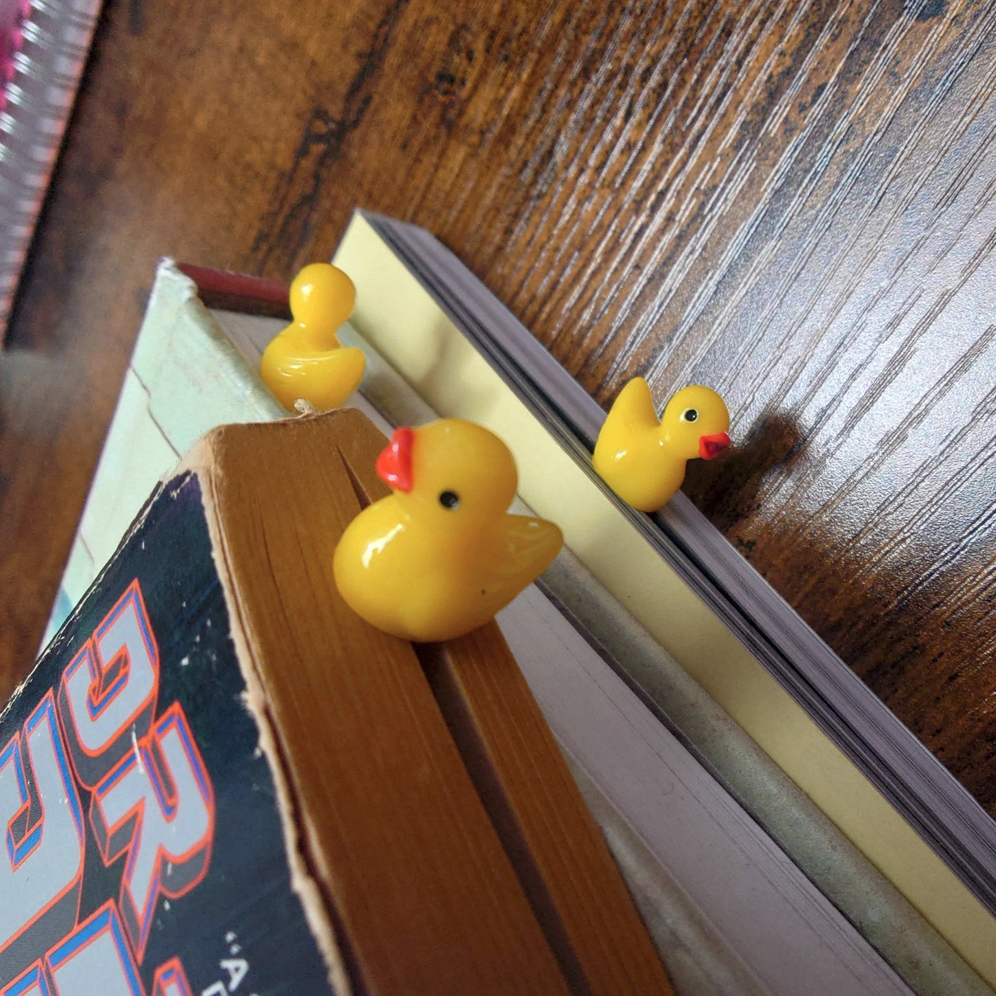 Three small yellow rubber ducks on a book with a wooden surface in the background