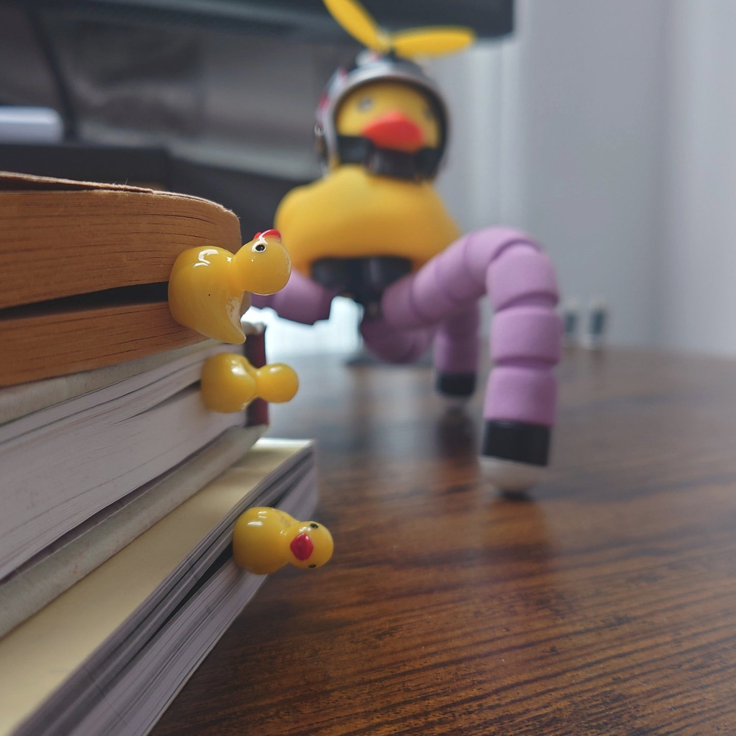 Three yellow rubber duck bookmarks on several books on a wooden table