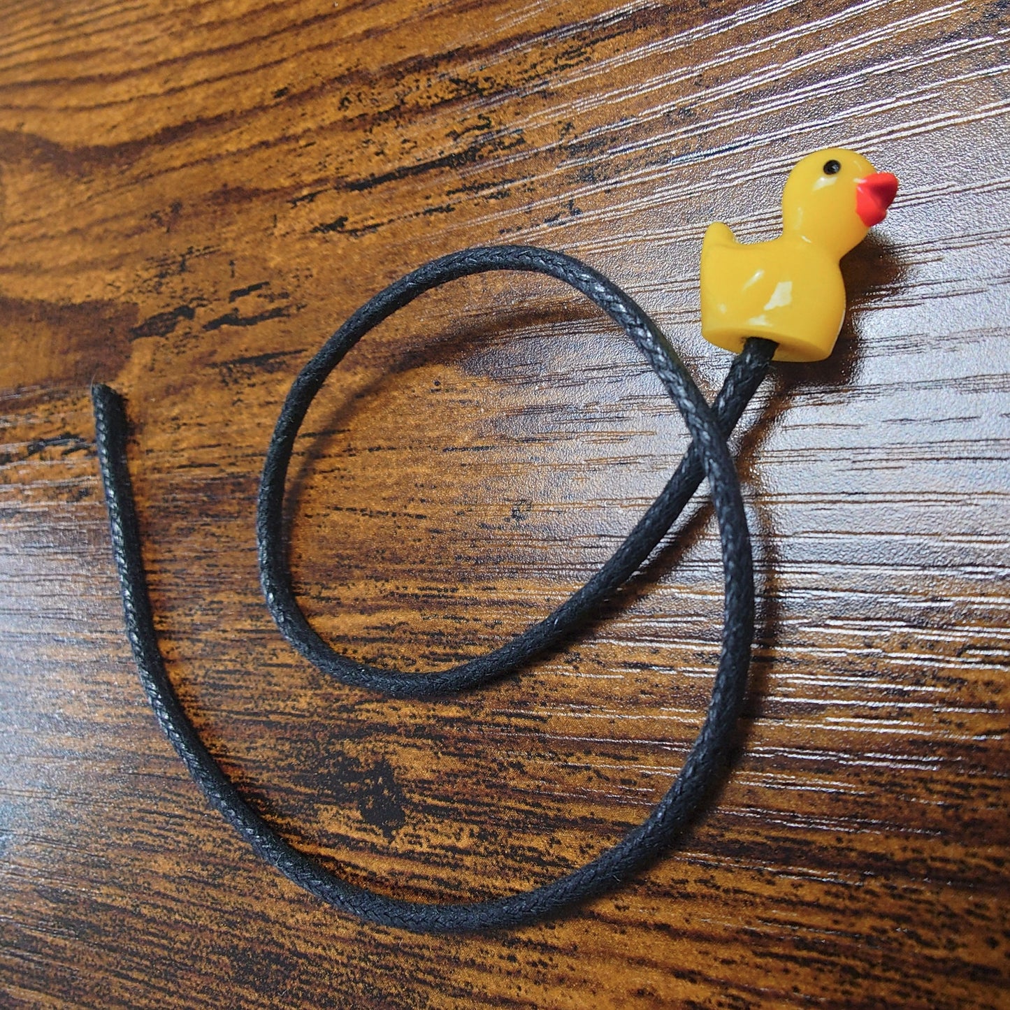 Yellow rubber duck bookmark with a black waxed cotton cord against a wooden background
