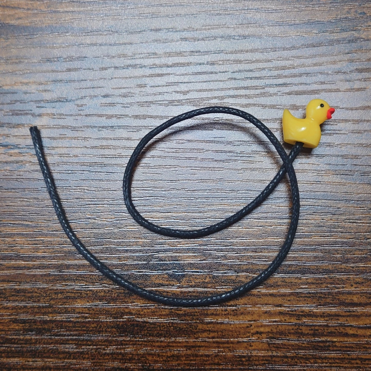A yellow rubber duck bookmark on a wooden background with black waxed cotton cord.