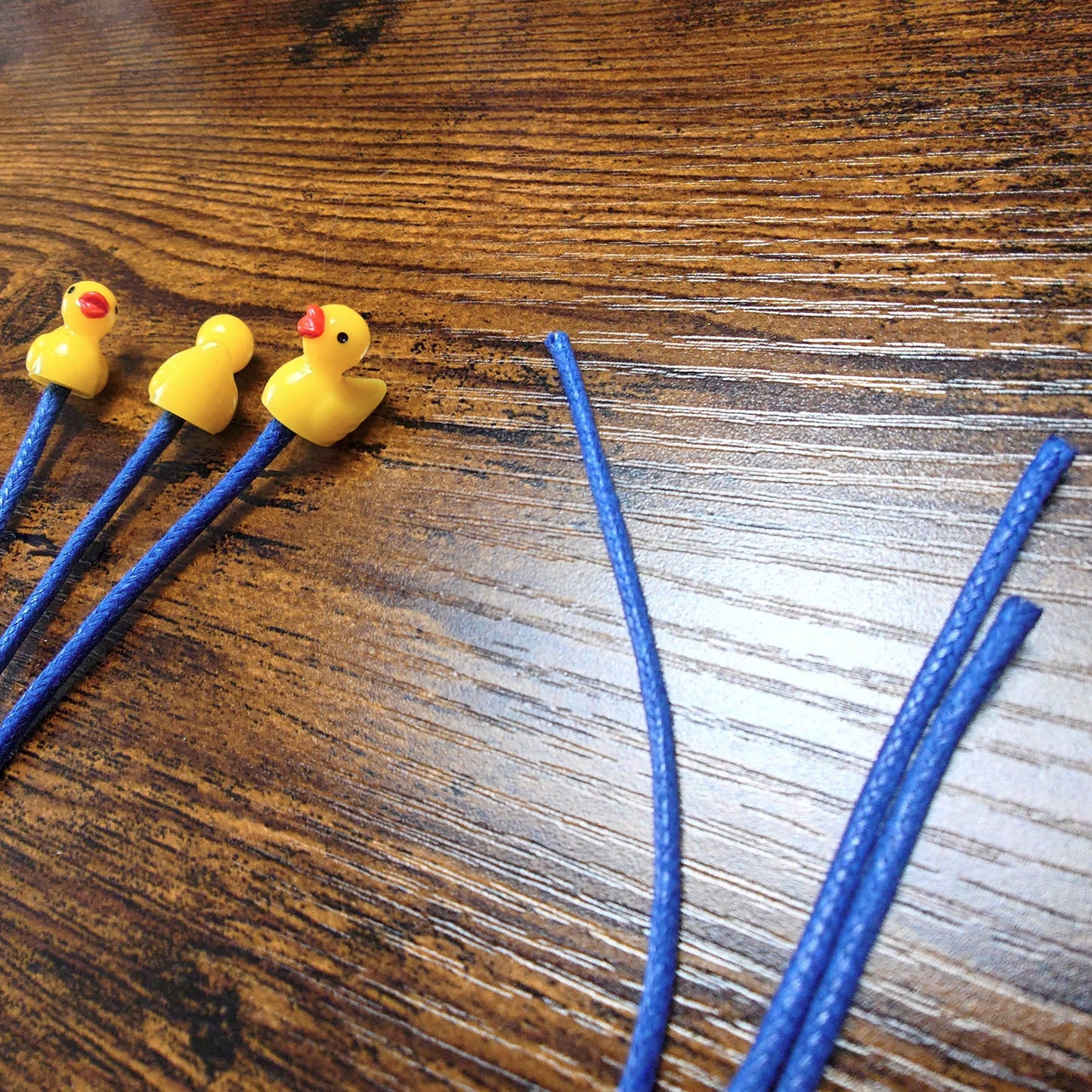 Three yellow rubber duck bookmarks on a wooden background with blue waxed cotton cord.