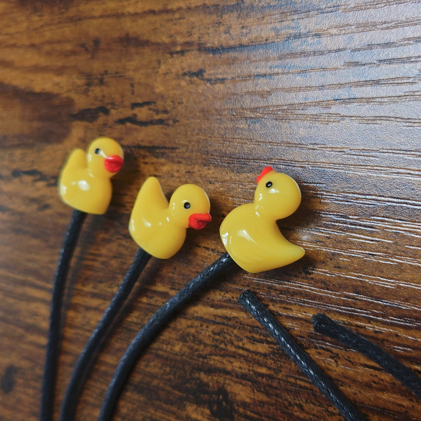 Three yellow rubber duck bookmarks on a wooden background with black waxed cotton cord.