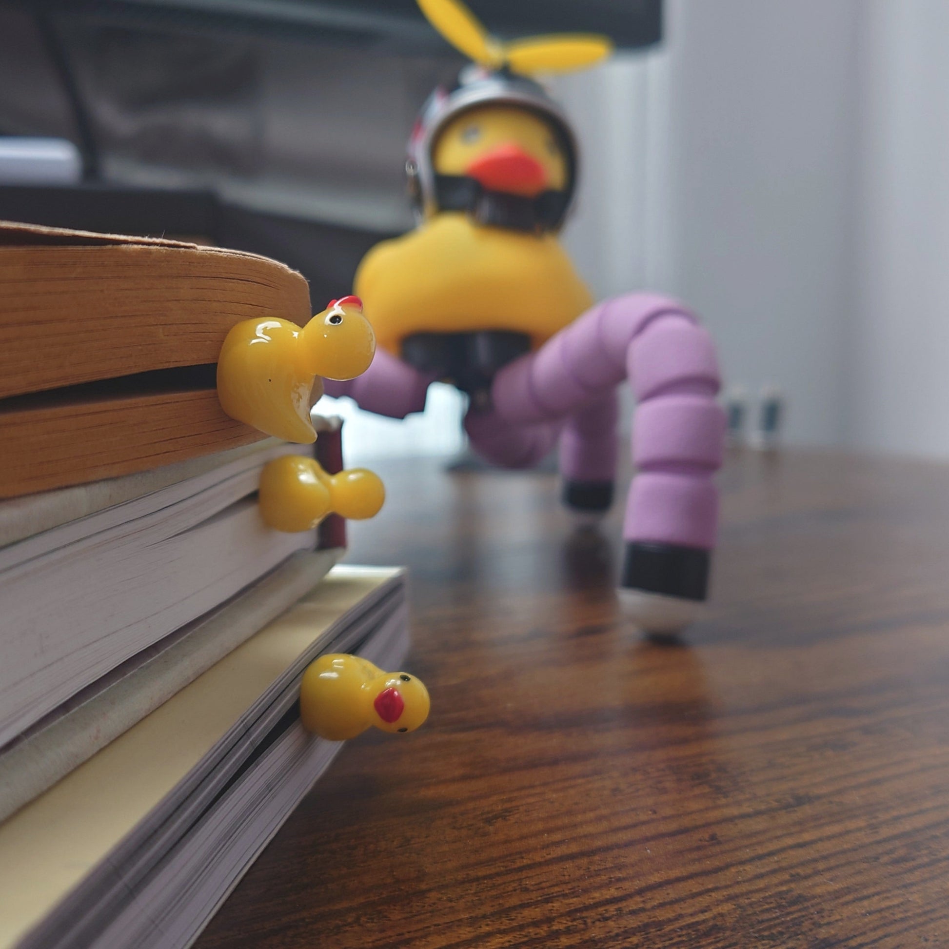 Three yellow rubber duck bookmarks on several books on a wooden table