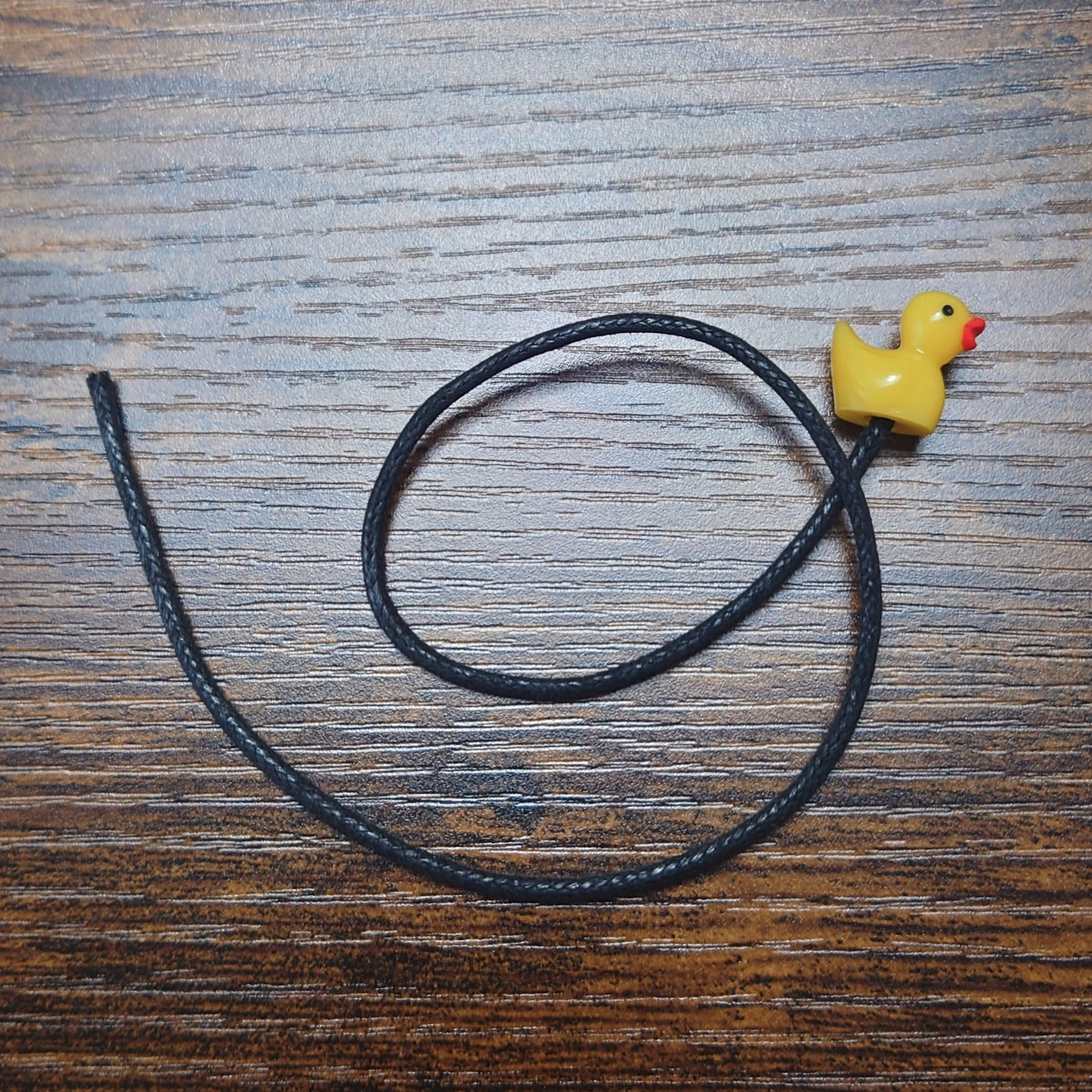 A yellow rubber duck bookmark on a wooden background with black waxed cotton cord.